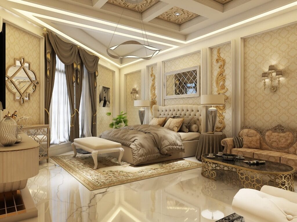 Elegant bedroom with gold accents, tufted headboard, chandeliers, and a cozy seating area.
